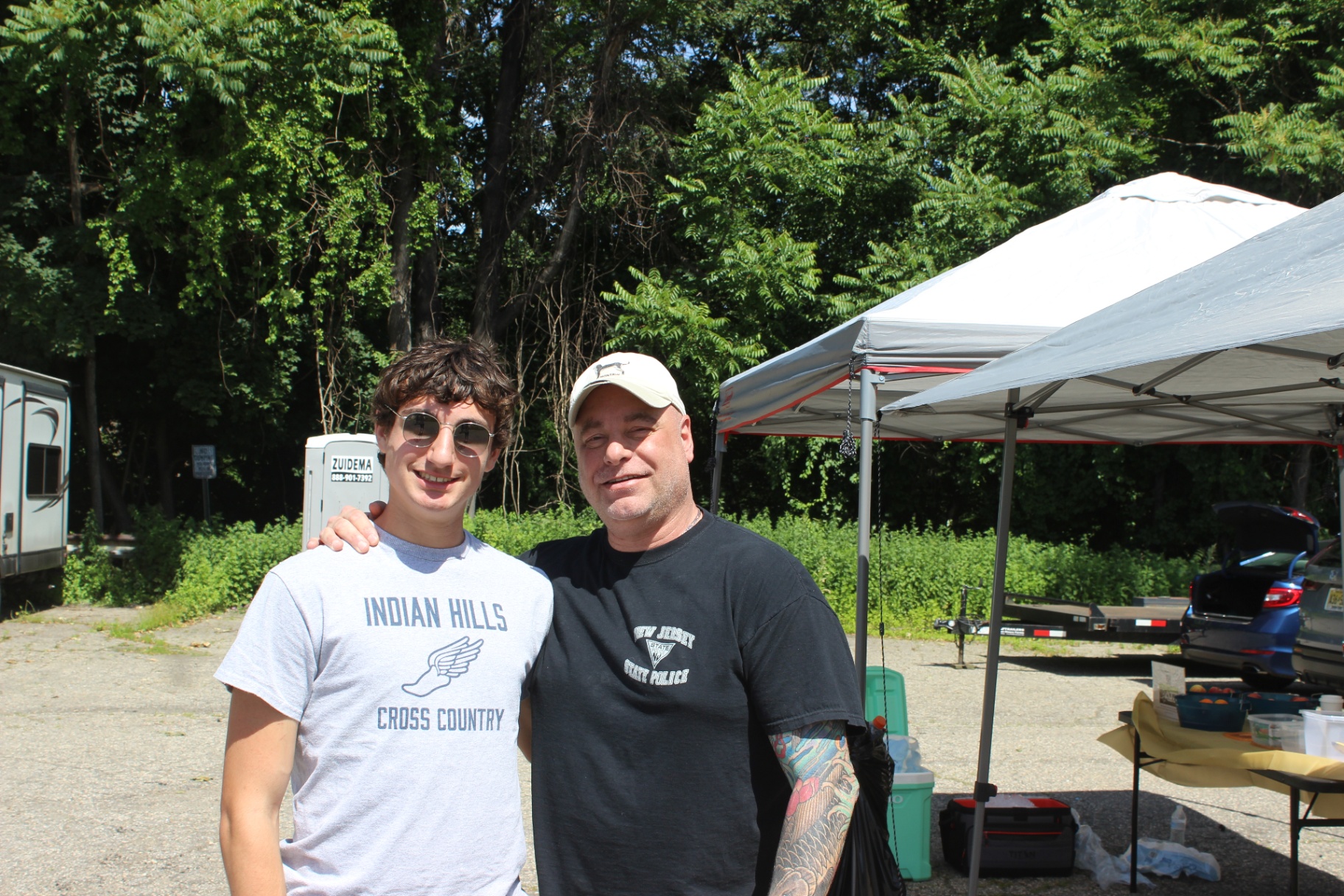 Two people smiling together at the Heart of Gold 5K event area on a sunny race day.