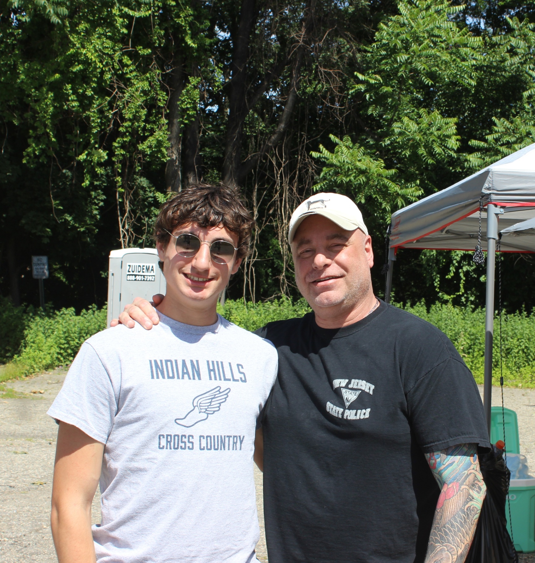 Two people smiling together at the Heart of Gold 5K event area on a sunny race day.