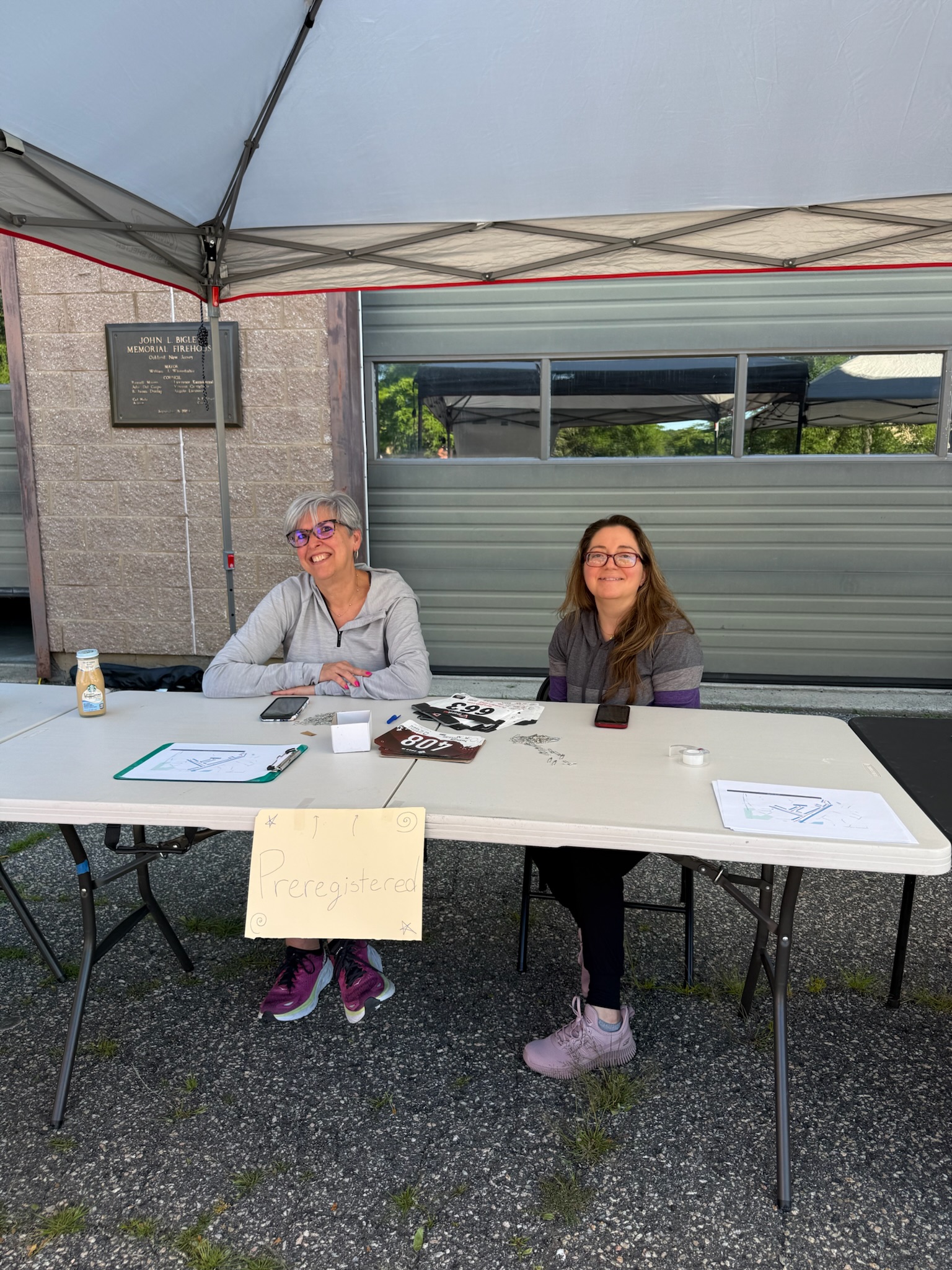 Two volunteers seated at the registration table under the event tent at the Heart of Gold 5K.