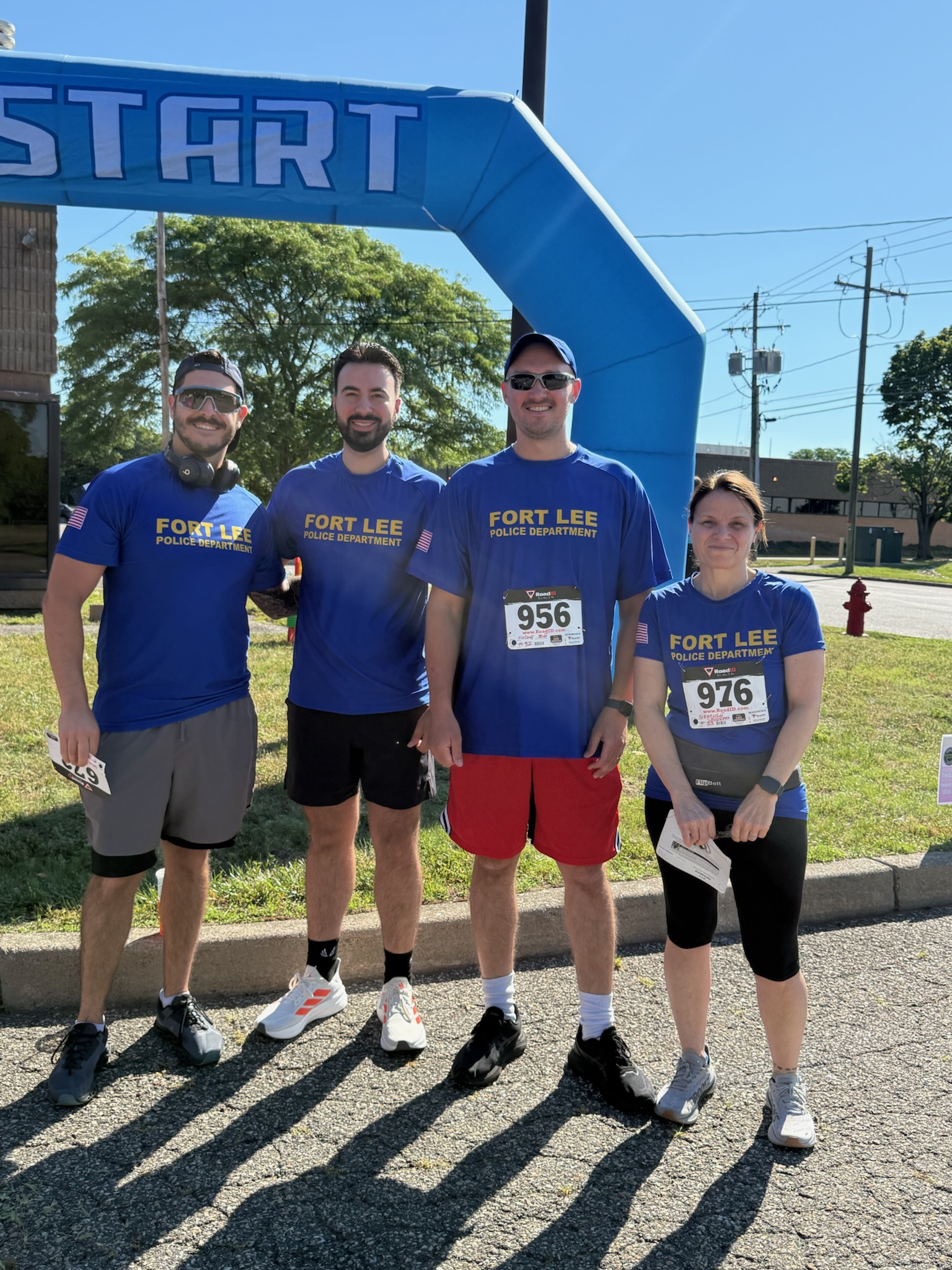 A group of race participants with numbered bibs posing beneath the Heart of Gold 5K start arch.